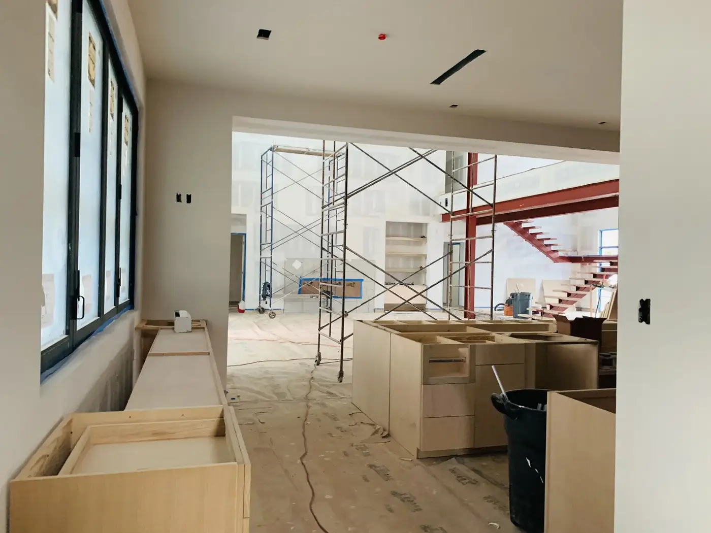 Interior renovation with black-framed windows, scaffolding, a red steel staircase, and unfinished cabinetry